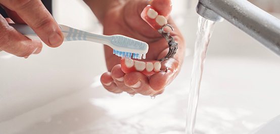 Hands brushing partial dentures under running tap water