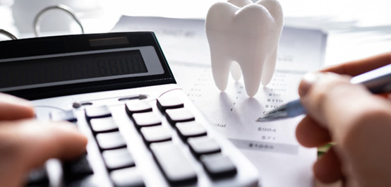 Hand holding pen and touching calculator at desk with model tooth and invoice