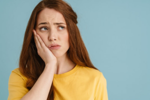 Woman holding a hand to her toothache on blue background