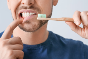 Close up of man holding toothbrush and pulling back lower lip to examine teeth